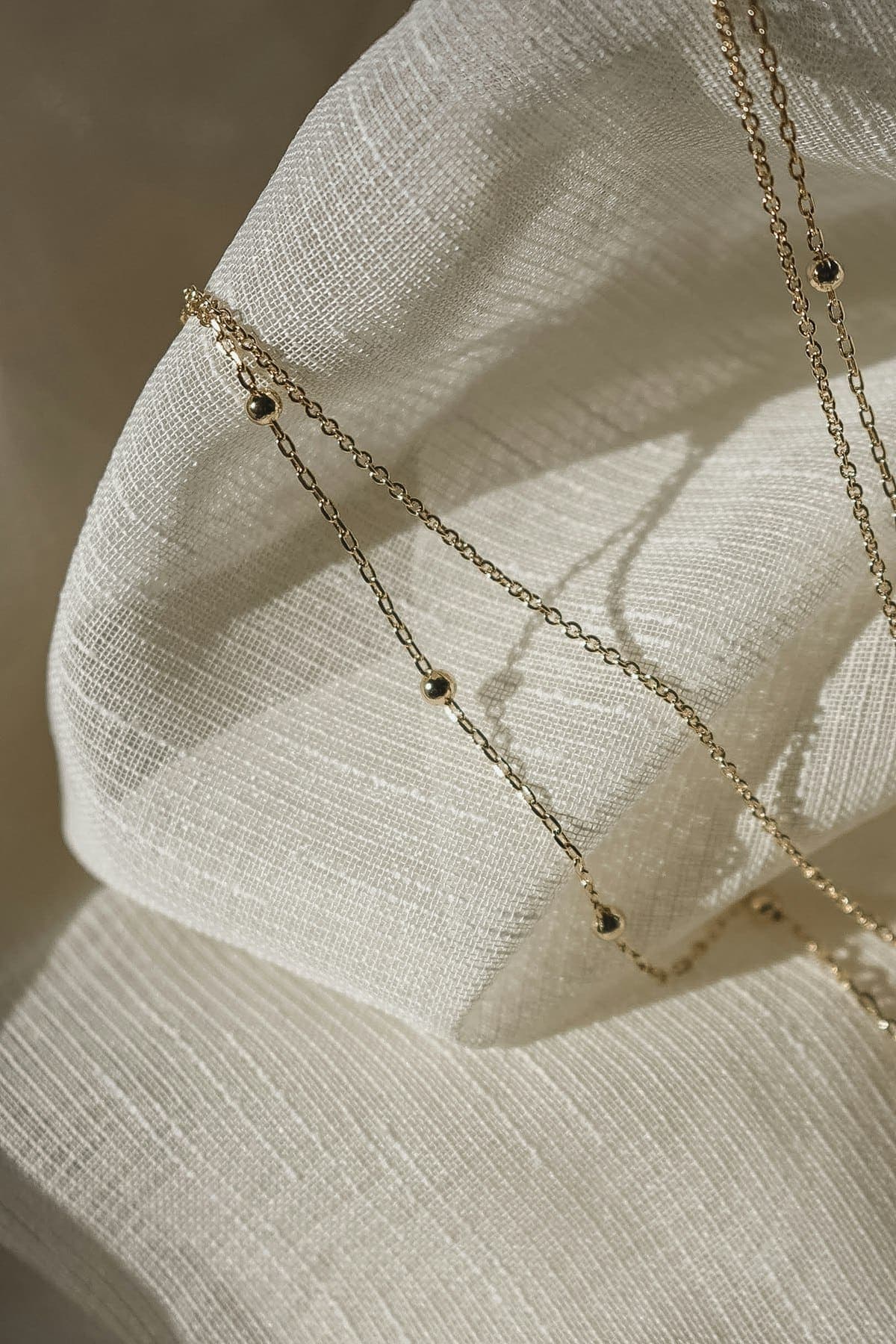 Two fine gold-tone chains on ivory fabric