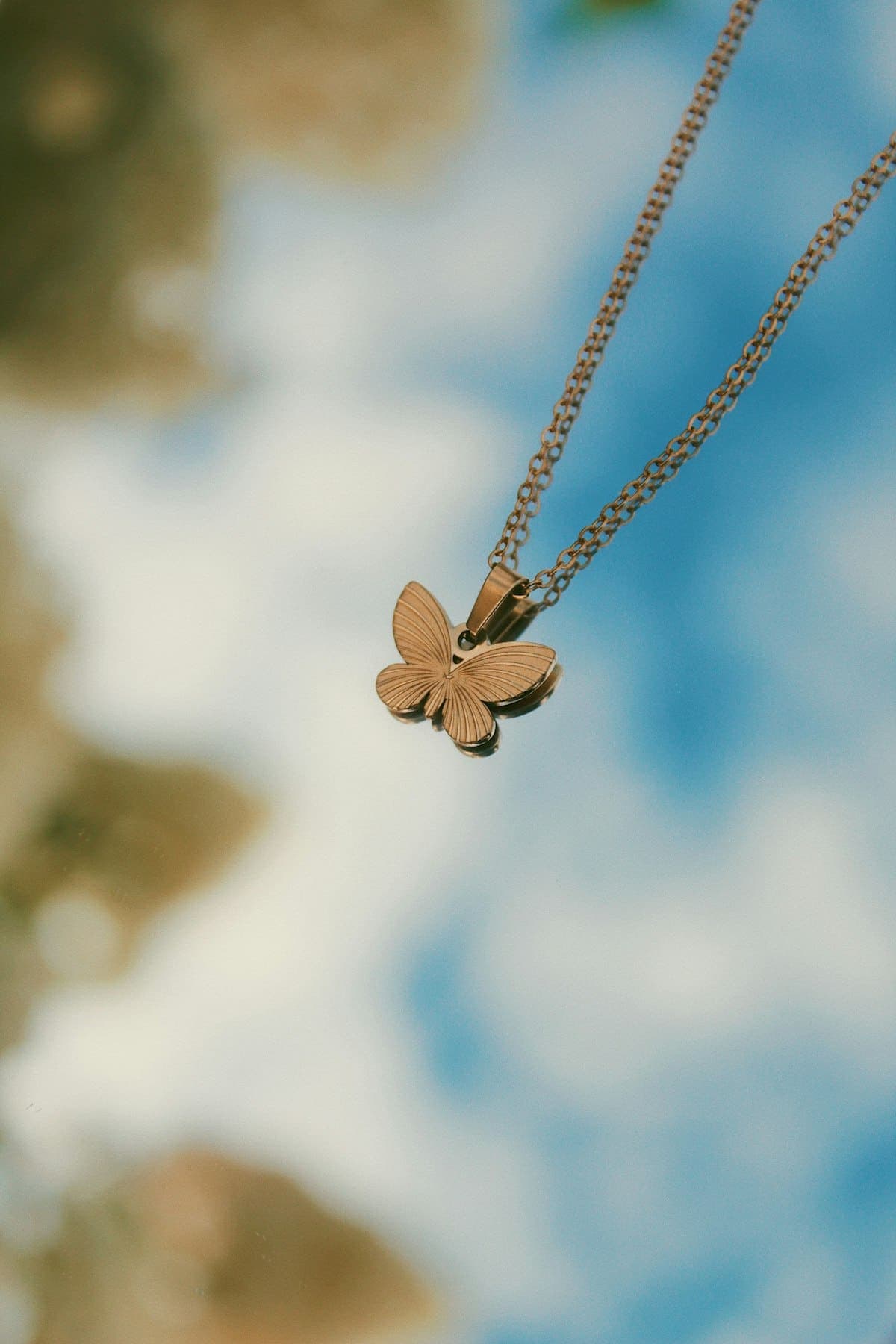 Rose-gold-tone butterfly pendant against the sky